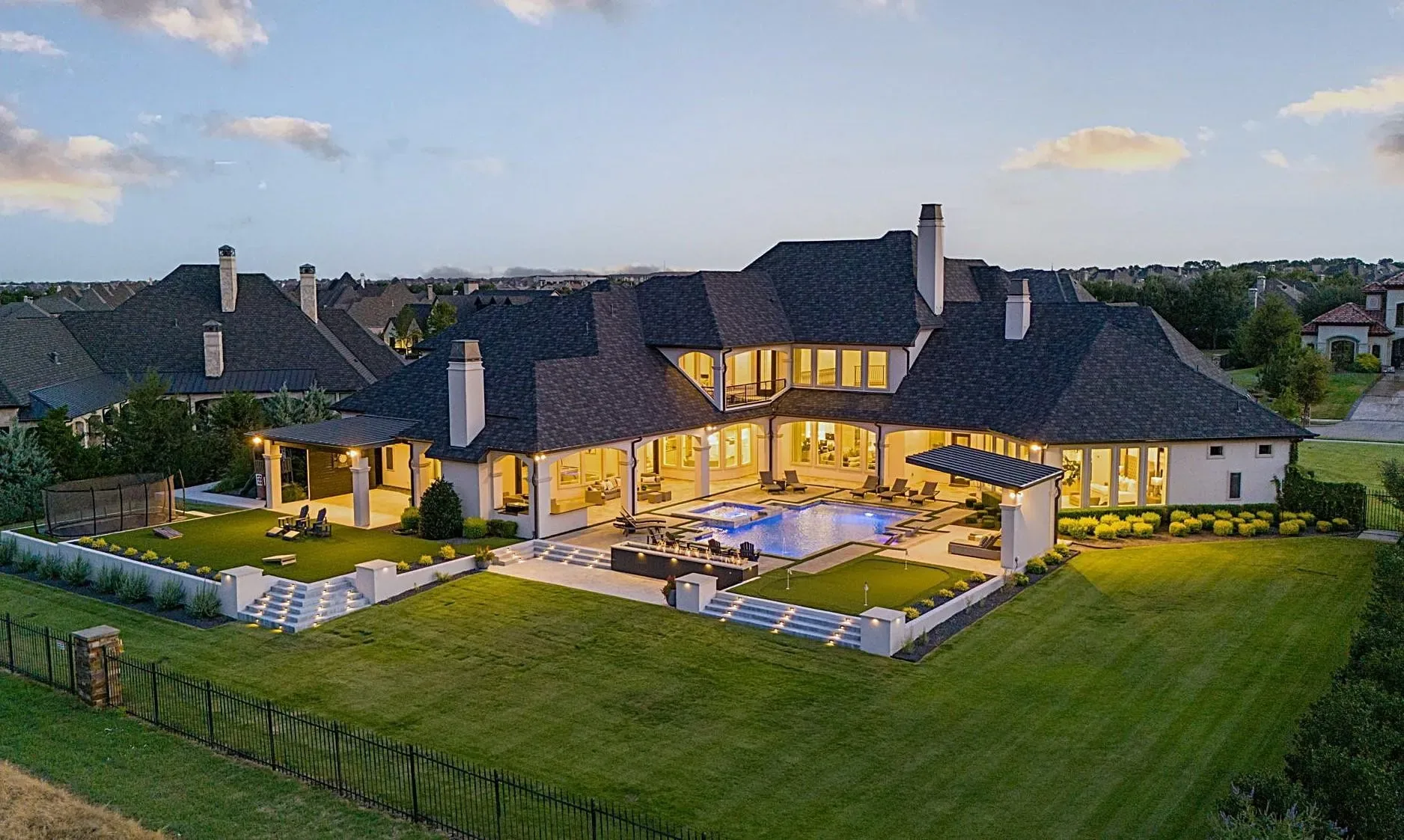 Aerial view at dusk of the rear yard, pool and lit covered patios of a large home at Craig Ranch, McKinney
