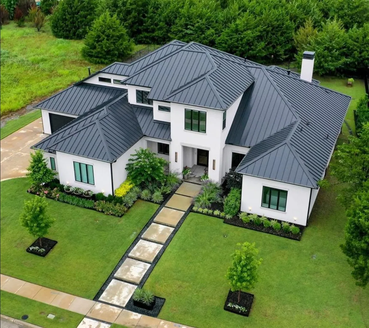 Aerial view of the front of a white modern home with a dark standing seam roof and a stepping-stone walk at Fairways of Heath Crossing