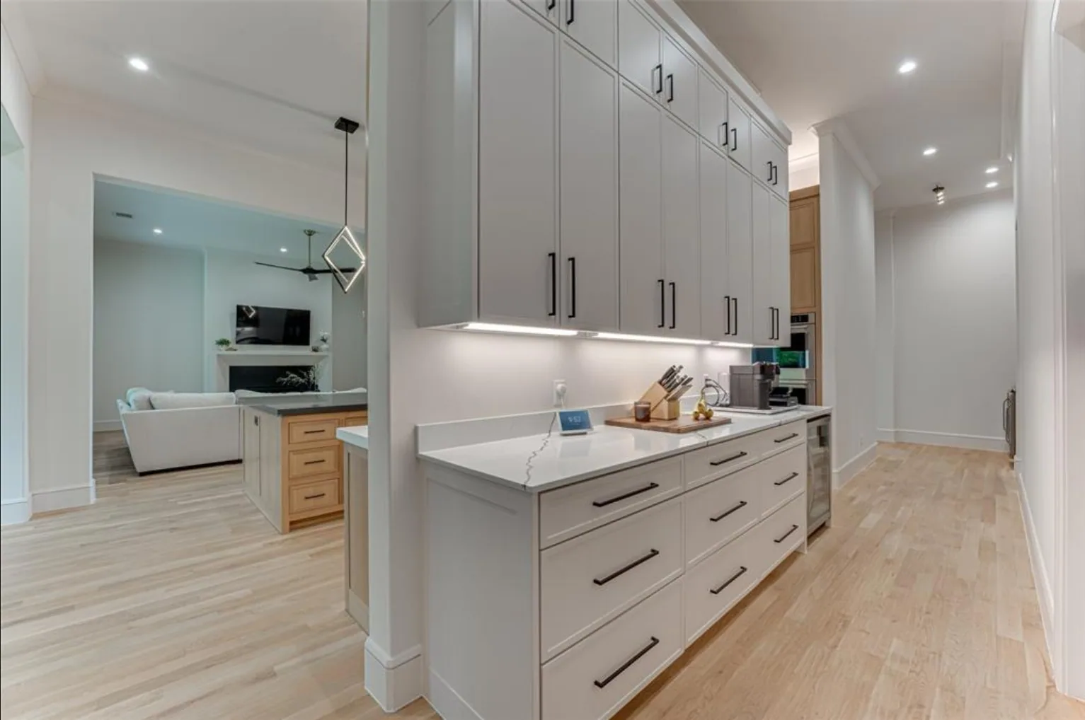Wall of tall white cabinets with under-cabinet lighting and a quartz counter beside the kitchen island at Fairways of Heath Crossing