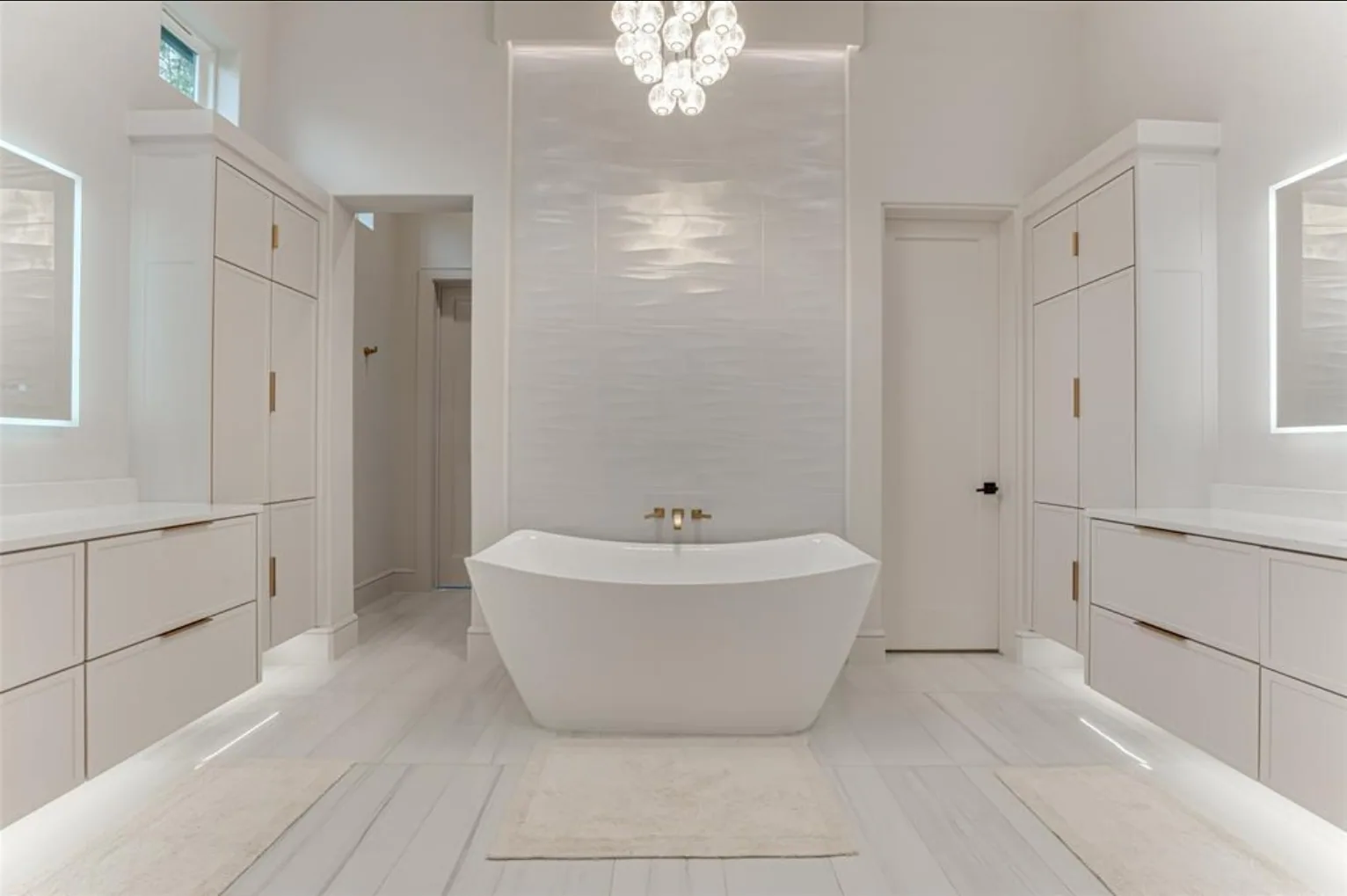 White primary bath with a freestanding tub against a tall textured tile wall and lit vanities on both sides at Fairways of Heath Crossing