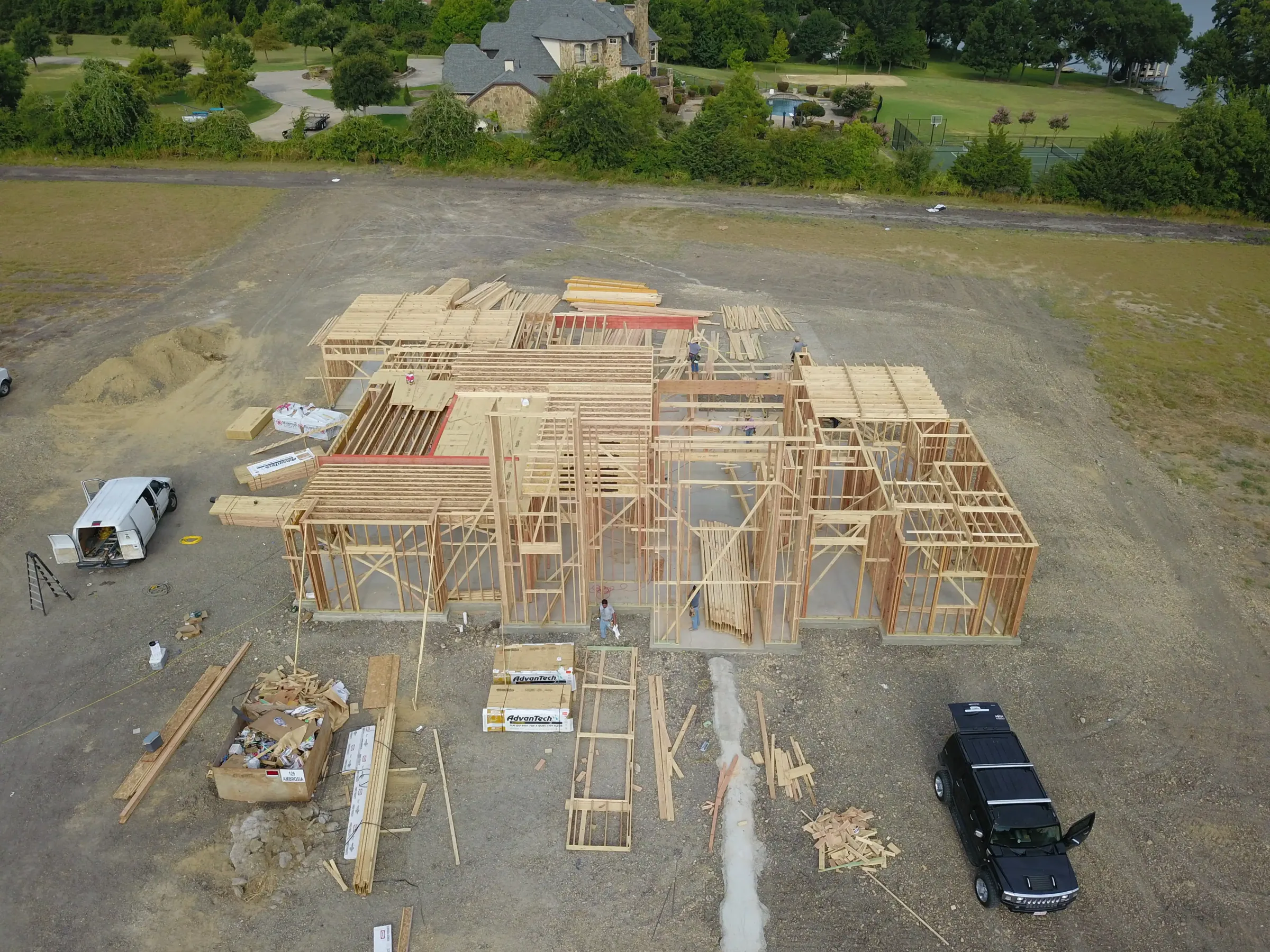 Aerial view of a custom home site across the lot, under work lights on a job site