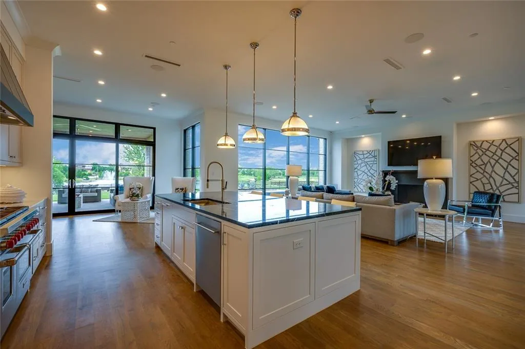 Open kitchen with a white island and pendant lights running into a living room with black steel-framed windows in Ridge Lakes of Heath