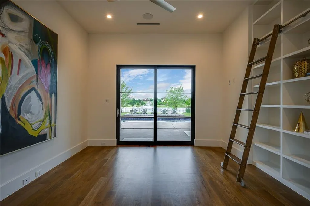 Study with built-in white shelving, a rolling library ladder and a black-framed glass door onto the pool in Ridge Lakes of Heath