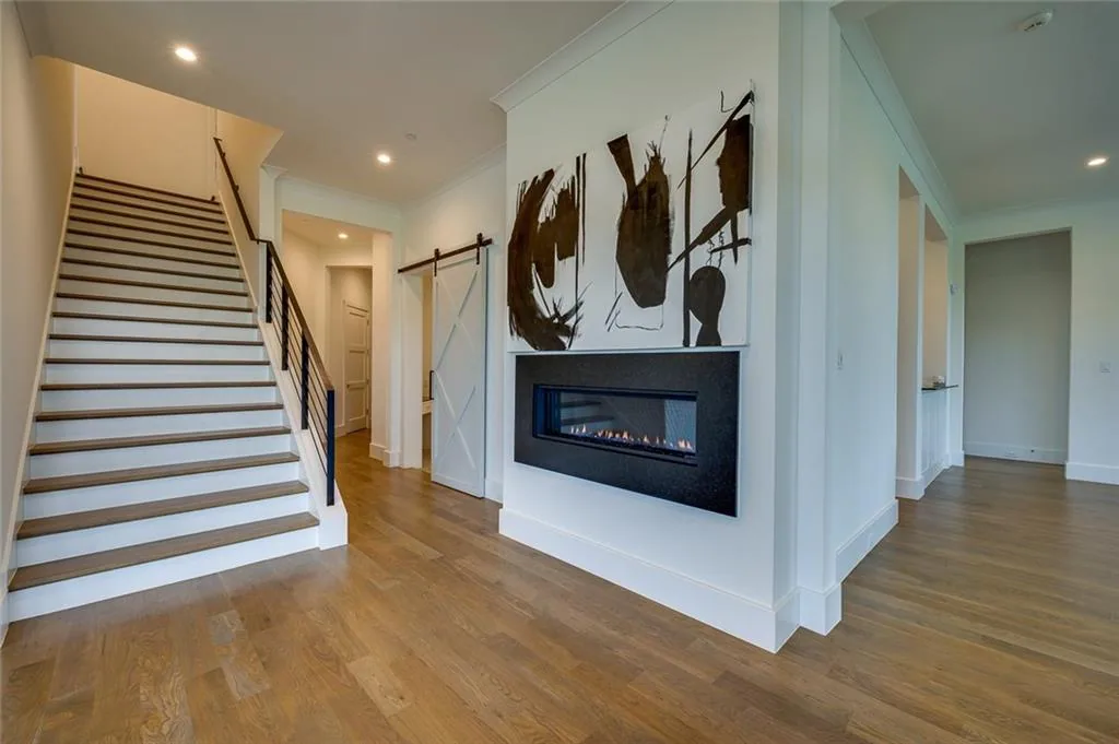 Straight stair rising beside a white wall with a linear gas fireplace and a sliding barn door in Ridge Lakes of Heath