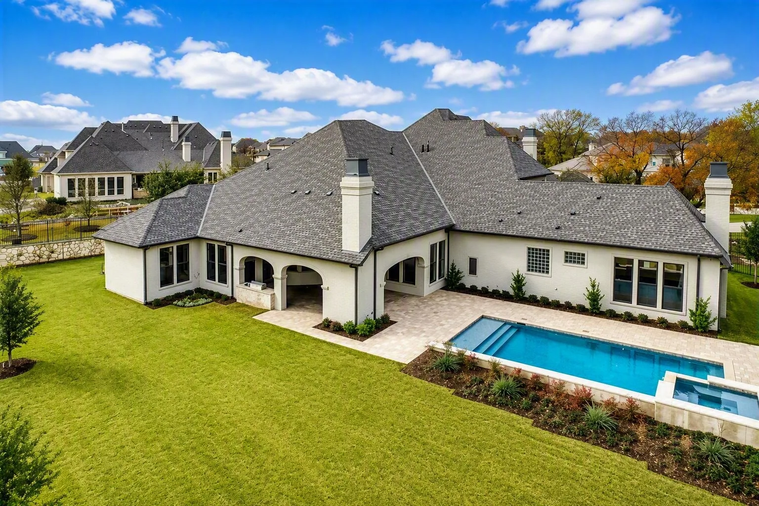 Aerial view of the rear of a white brick home with arched covered patios, a pool and a spa at Wimberly Place, Allen
